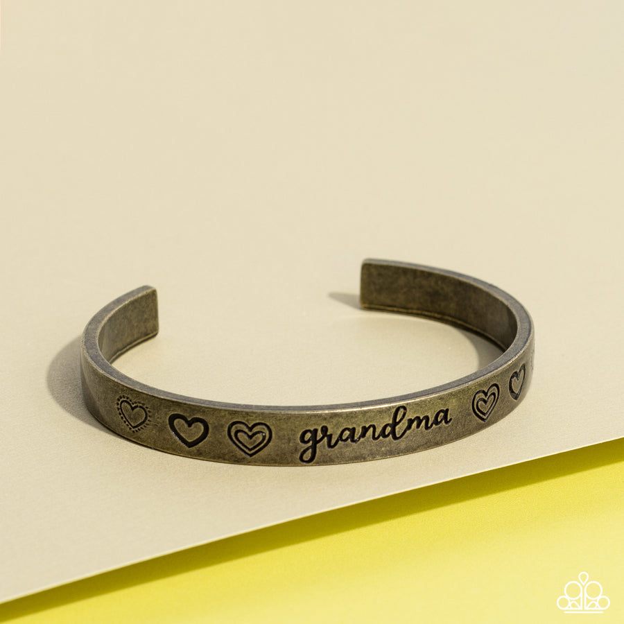 A Grandmothers Love - Brass Bracelet - Paparazzi Accessories - Brushed in an antiqued grit, a skinny brass bar curls around the wrist, creating a rustic cuff. Featuring a heart motif, the skinny cuff is engraved with the word “grandma” with various styles of hearts framing the word for an inspiring, heartfelt finish. Sold as one individual bracelet.