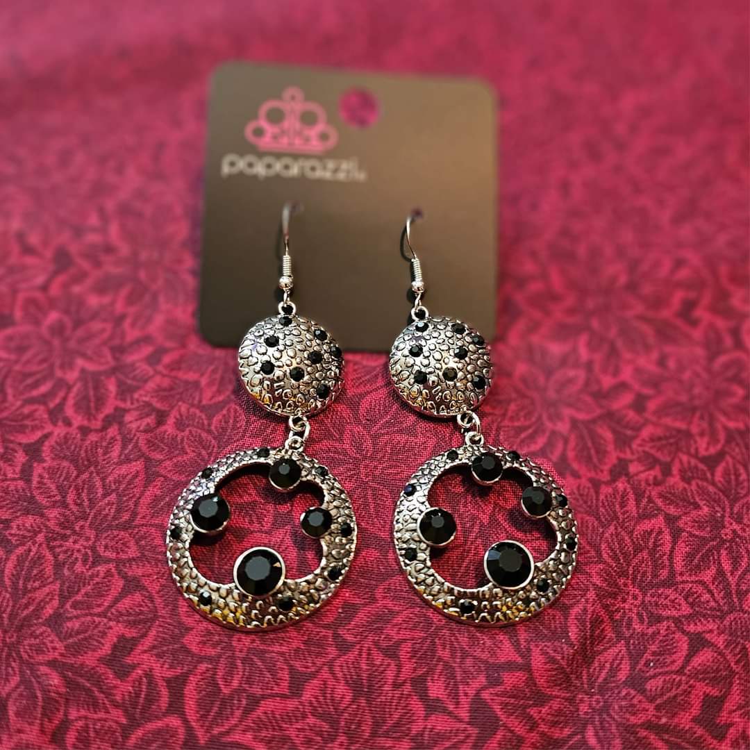 Eastern Entrada - Black and Silver Earrings - Paparazzi Accessories - Dotted with dainty black rhinestones and embossed in pebble-like textures, a beveled silver circle attaches to an imperfect silver hoop featuring matching texture. A smattering of oversized black rhinestones haphazardly adorns the hoop, resulting in a gritty shimmer.