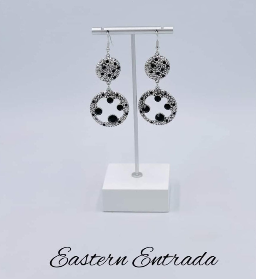 Eastern Entrada - Black and Silver Earrings - Paparazzi Accessories - Dotted with dainty black rhinestones and embossed in pebble-like textures, a beveled silver circle attaches to an imperfect silver hoop featuring matching texture. A smattering of oversized black rhinestones haphazardly adorns the hoop, resulting in a gritty shimmer.