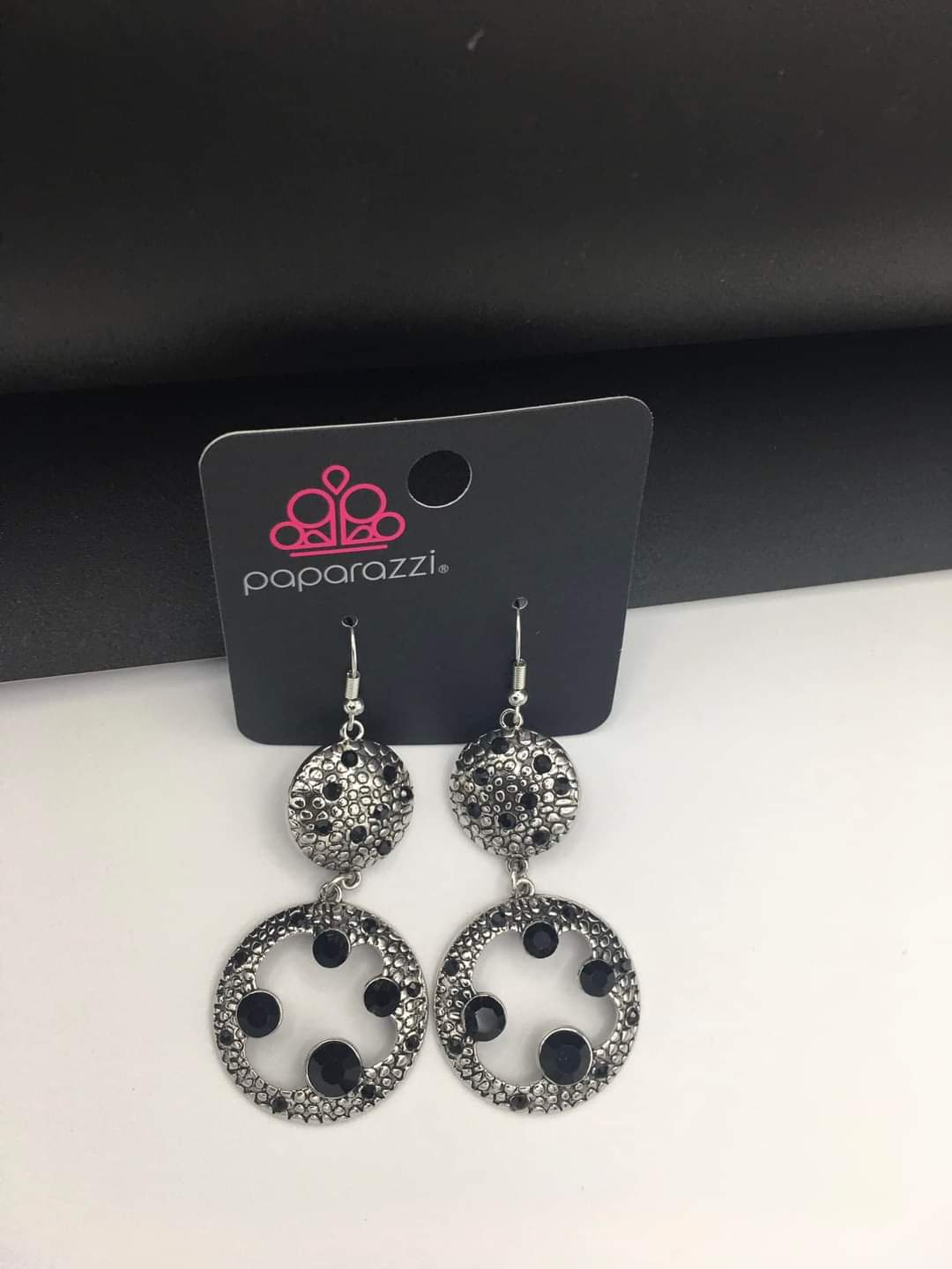 Eastern Entrada - Black and Silver Earrings - Paparazzi Accessories - Dotted with dainty black rhinestones and embossed in pebble-like textures, a beveled silver circle attaches to an imperfect silver hoop featuring matching texture. A smattering of oversized black rhinestones haphazardly adorns the hoop, resulting in a gritty shimmer.